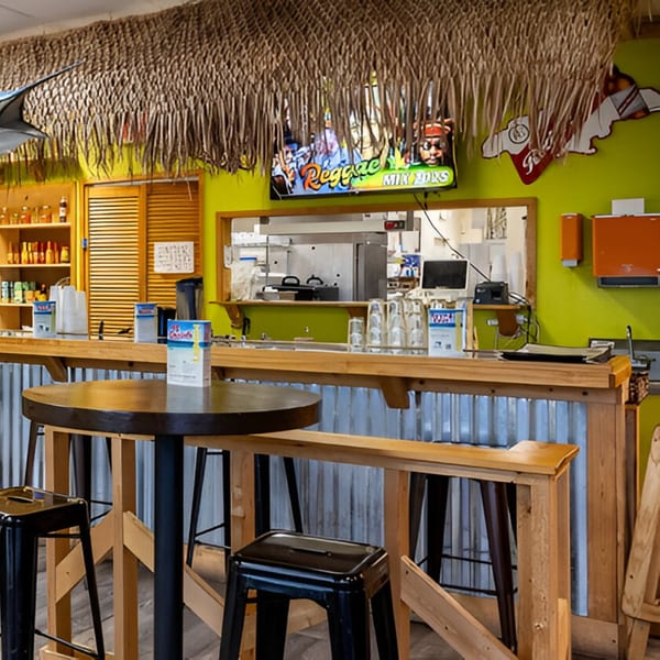 Interior of Da Blue Lagoon Jamaican Kitchen, featuring a bar with stools and a thatched roof.