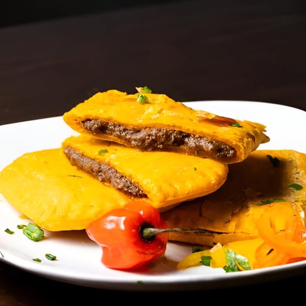 Golden Jamaican patties filled with savory meat, garnished with a red pepper and herbs.