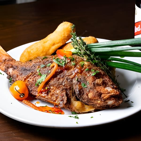 Whole fried fish with bammy, garnished with herbs, peppers, and scallions on a white plate.